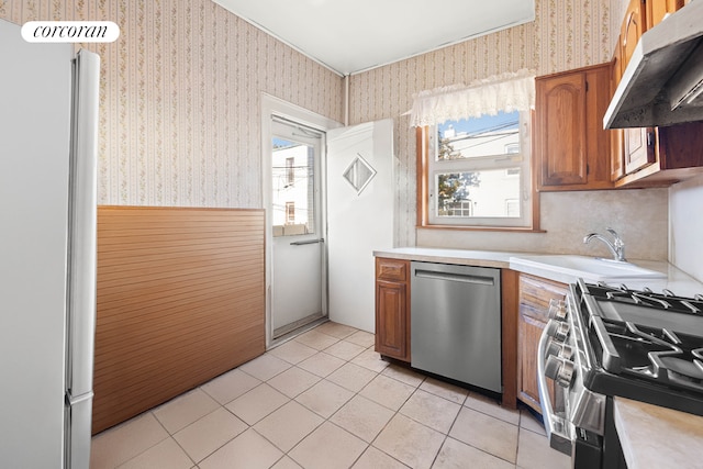 kitchen featuring wallpapered walls, under cabinet range hood, stainless steel appliances, and wainscoting