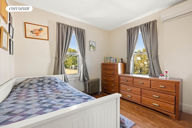 bedroom with radiator, a wall mounted air conditioner, and wood finished floors