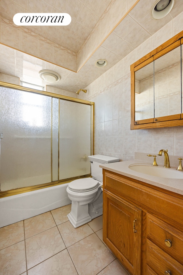 bathroom with toilet, tile patterned floors, combined bath / shower with glass door, vanity, and tile walls