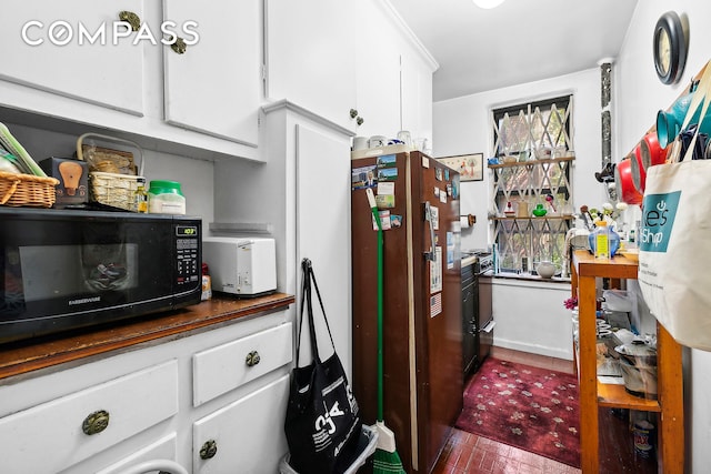 kitchen featuring white cabinets, freestanding refrigerator, and black microwave