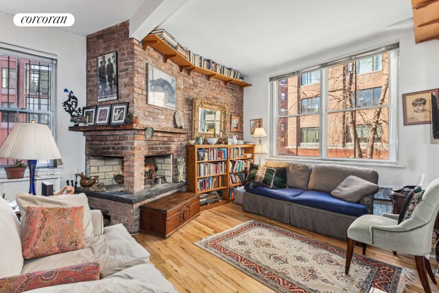 living area with a brick fireplace, visible vents, beam ceiling, and wood finished floors