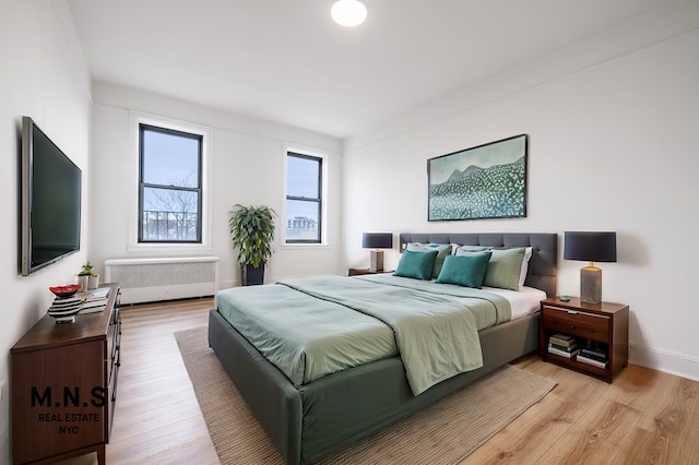 bedroom featuring baseboards, light wood finished floors, and radiator heating unit