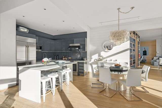 kitchen featuring appliances with stainless steel finishes, backsplash, light wood-style flooring, and under cabinet range hood