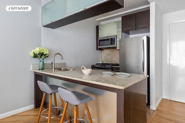 kitchen featuring light wood-type flooring, a sink, backsplash, appliances with stainless steel finishes, and a breakfast bar area