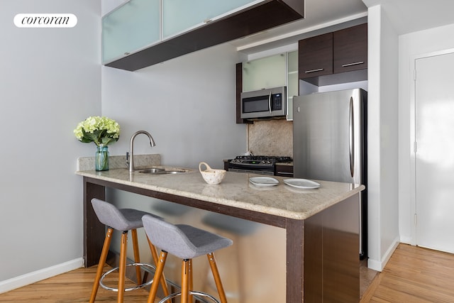 kitchen featuring a kitchen bar, light wood-type flooring, a sink, baseboards, and stainless steel appliances