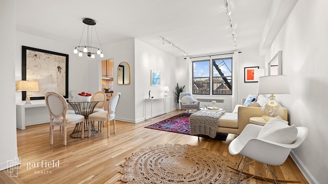 living area with a notable chandelier, rail lighting, radiator heating unit, wood finished floors, and baseboards