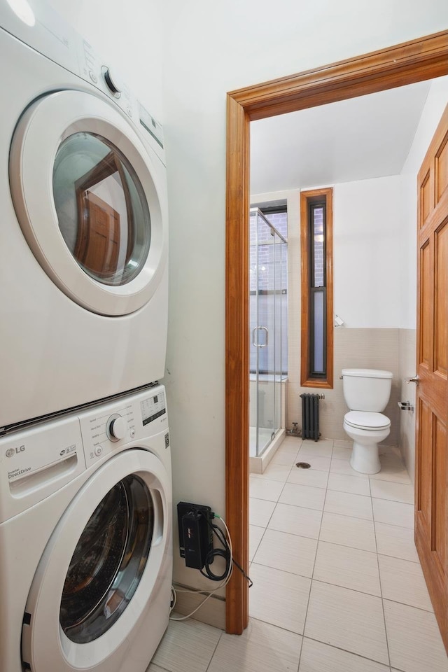 laundry room featuring laundry area, radiator heating unit, light tile patterned floors, and stacked washer / dryer