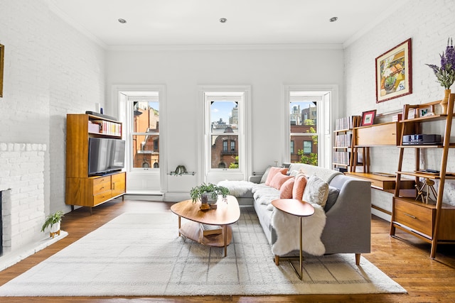 living area with brick wall, a fireplace, ornamental molding, and wood finished floors