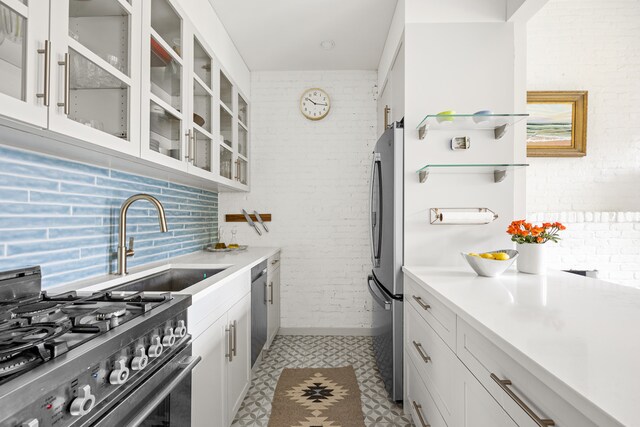 kitchen featuring brick wall, appliances with stainless steel finishes, light countertops, white cabinetry, and a sink