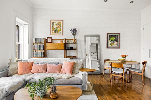 living room featuring brick wall, crown molding, and dark wood-type flooring