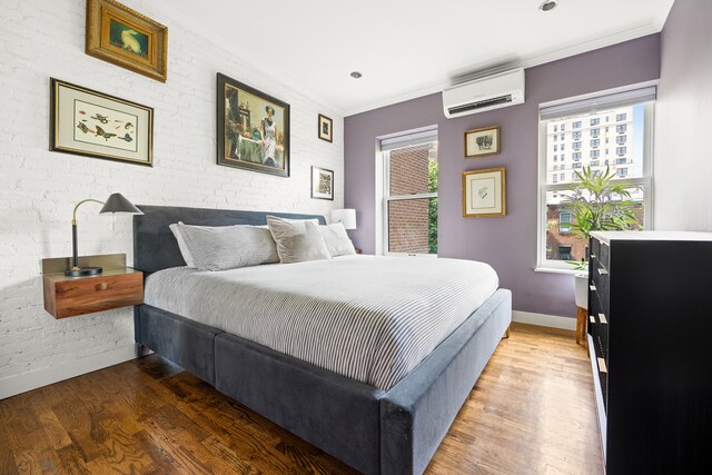 bedroom featuring brick wall, multiple windows, wood finished floors, and a wall mounted air conditioner