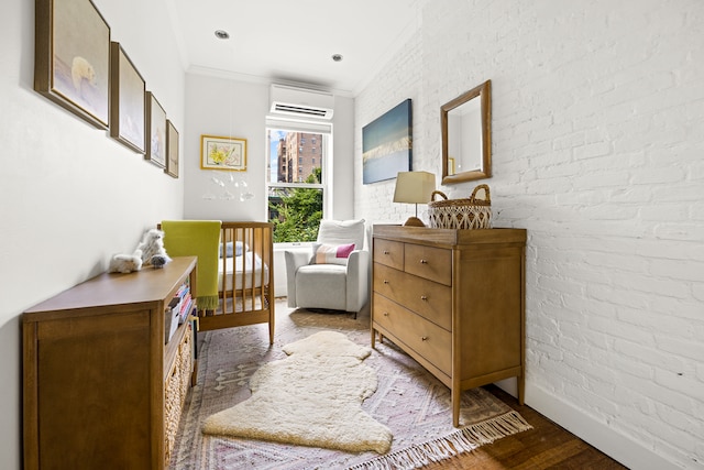 sitting room featuring ornamental molding, an AC wall unit, brick wall, wood finished floors, and baseboards