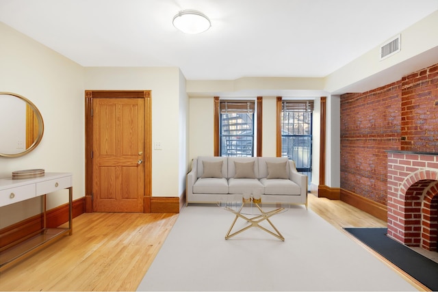 living room with baseboards, visible vents, brick wall, wood finished floors, and a brick fireplace