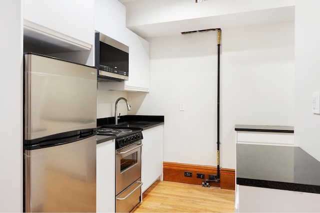 kitchen featuring a sink, white cabinets, appliances with stainless steel finishes, light wood-type flooring, and dark countertops