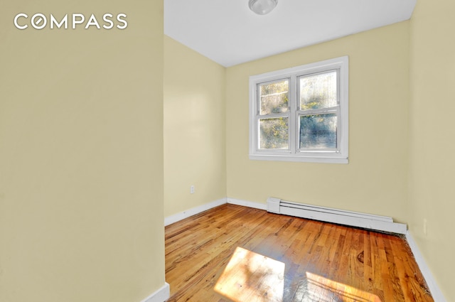 spare room featuring a baseboard heating unit, wood finished floors, and baseboards