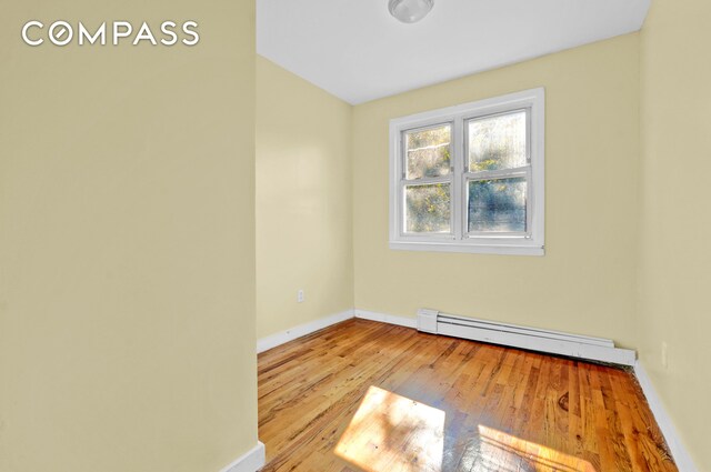 empty room featuring baseboards, a baseboard radiator, and wood-type flooring