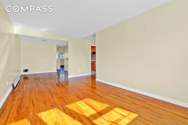 empty room featuring light wood-style floors, baseboards, and baseboard heating