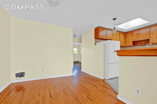 kitchen with light wood-type flooring, a skylight, freestanding refrigerator, and baseboards