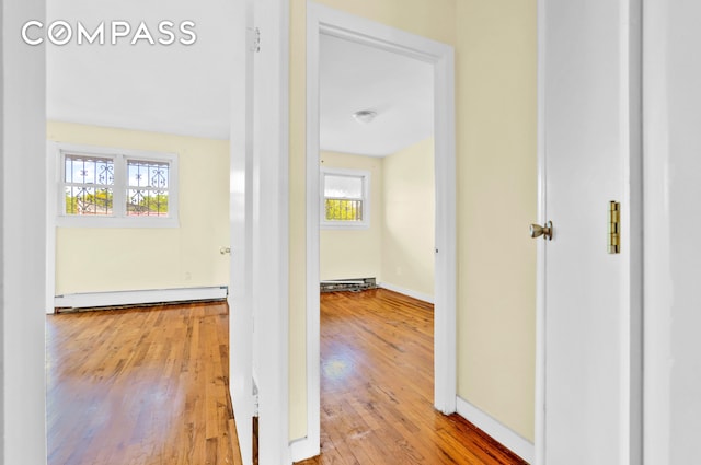 hallway with wood-type flooring, a baseboard radiator, baseboards, and a healthy amount of sunlight