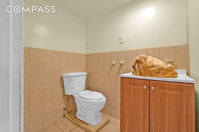 half bath with tile walls, tile patterned flooring, wainscoting, vanity, and toilet