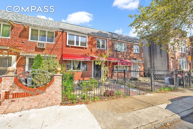 townhome / multi-family property featuring a fenced front yard, roof with shingles, and brick siding