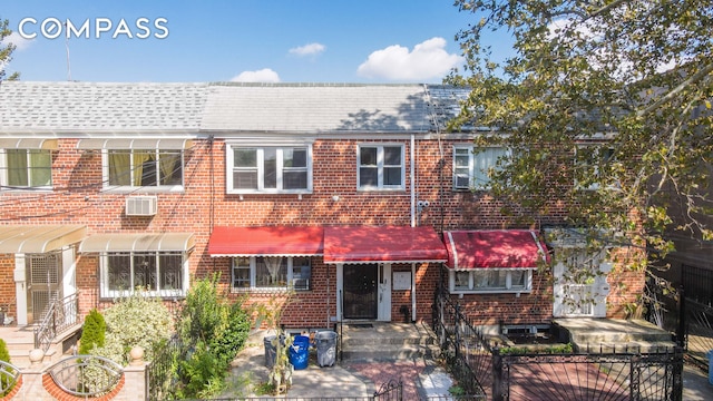 townhome / multi-family property with a fenced front yard, brick siding, and a wall unit AC