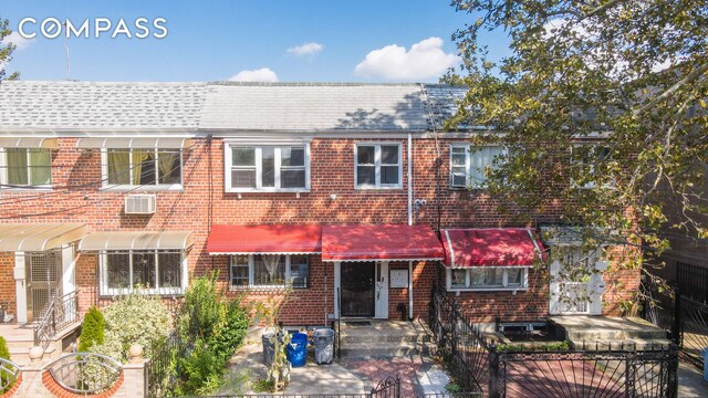 view of front facade featuring roof with shingles, a wall mounted AC, fence private yard, and brick siding