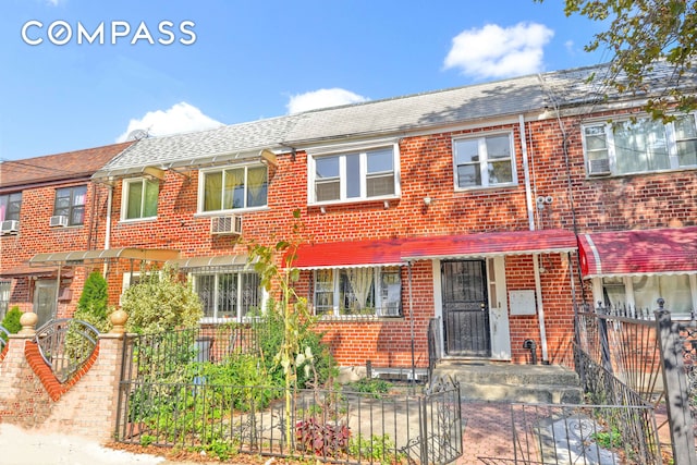 townhome / multi-family property featuring brick siding, a fenced front yard, and roof with shingles