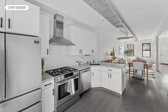 kitchen with wall chimney range hood, dark wood finished floors, open floor plan, appliances with stainless steel finishes, and a peninsula