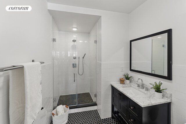 bathroom with a wainscoted wall, tile walls, a shower stall, vanity, and tile patterned floors