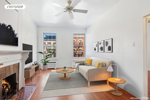 living room with baseboards, visible vents, a tiled fireplace, ceiling fan, and wood finished floors