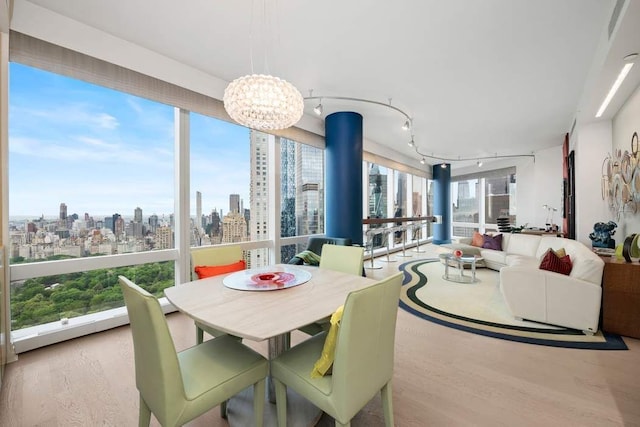 dining space featuring track lighting, an inviting chandelier, wood finished floors, and a city view