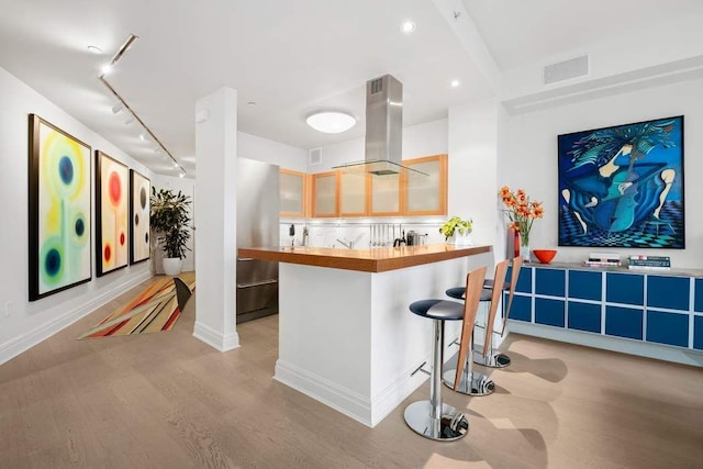 kitchen featuring island exhaust hood, light wood finished floors, track lighting, a kitchen breakfast bar, and baseboards