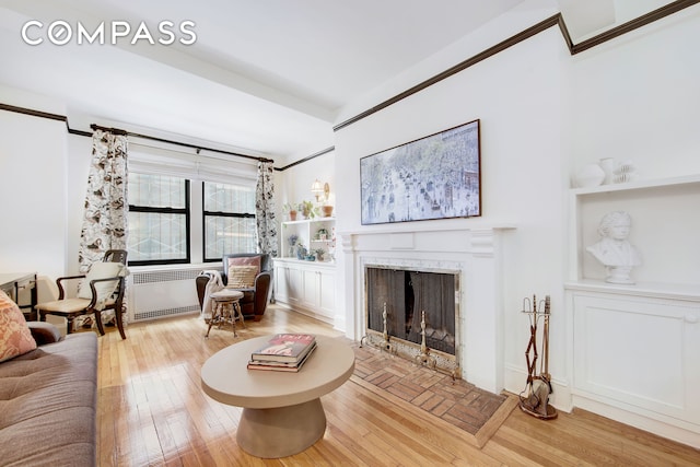 living area with a fireplace with flush hearth, radiator, and hardwood / wood-style floors