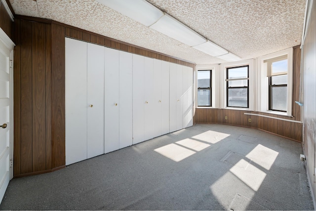 unfurnished bedroom featuring wooden walls, carpet, and multiple windows