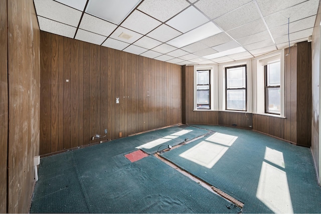 unfurnished room with carpet, a drop ceiling, and wooden walls