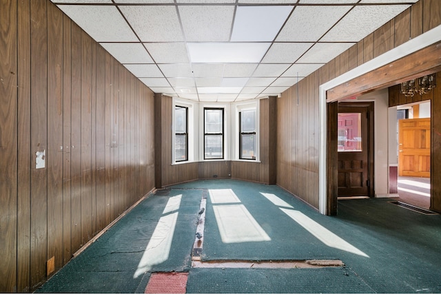 carpeted spare room with a paneled ceiling and wooden walls