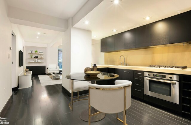 kitchen with stovetop, dark wood finished floors, dark cabinetry, and oven