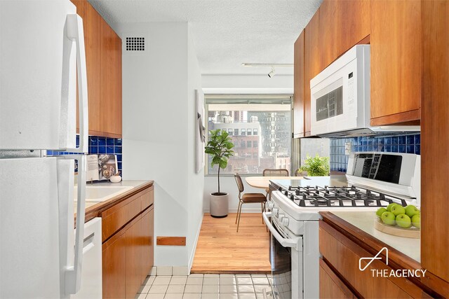 170 Park Row Unit 7C, New York City, NY 10038 - kitchen with white appliances, light tile patterned flooring, brown cabinets, light countertops, and tasteful backsplash