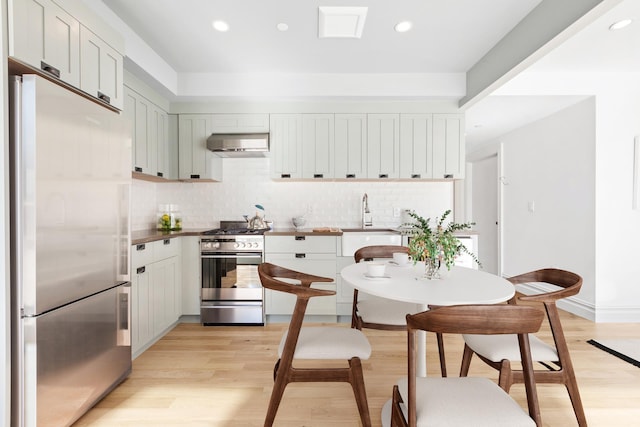 kitchen with appliances with stainless steel finishes, tasteful backsplash, light wood-style flooring, and exhaust hood