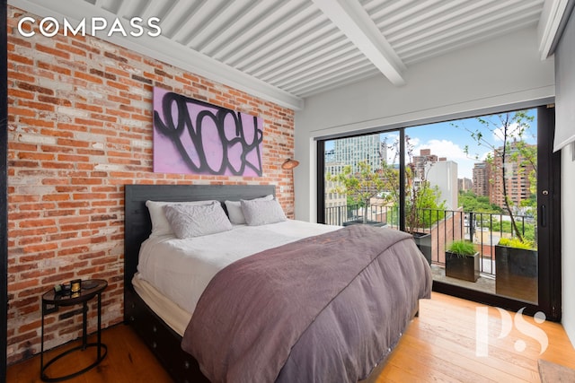 bedroom featuring beamed ceiling, wood-type flooring, a city view, and access to exterior