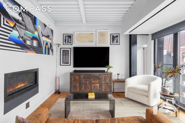 living area featuring beam ceiling, a glass covered fireplace, and wood finished floors