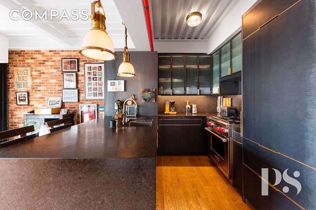 kitchen featuring dark countertops, brick wall, high quality appliances, light wood-style flooring, and a sink