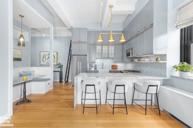 kitchen featuring stainless steel appliances, a peninsula, backsplash, light wood finished floors, and beamed ceiling