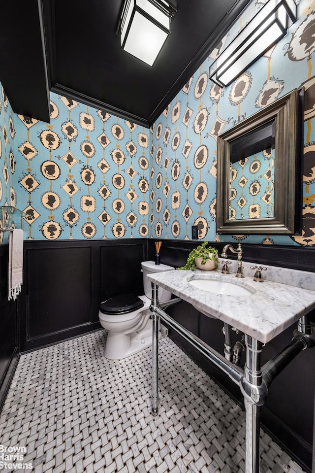 half bath with wallpapered walls, crown molding, a sink, and a wainscoted wall