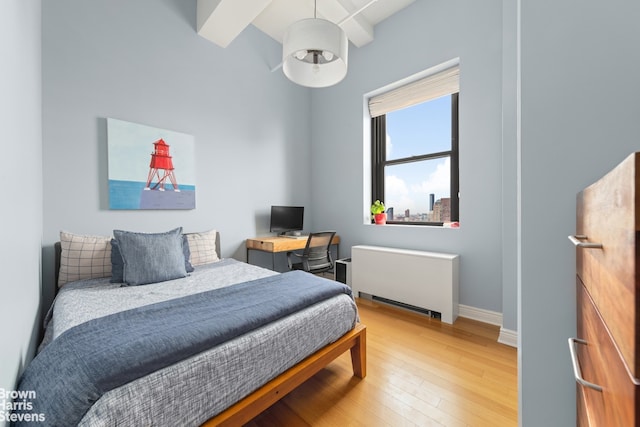 bedroom featuring hardwood / wood-style floors, radiator heating unit, beam ceiling, and baseboards