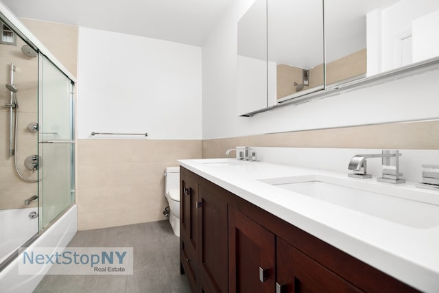 245 E 54th St Unit 19K, New York City, NY 10022 - bathroom with tile walls, toilet, double vanity, bath / shower combo with glass door, and wainscoting