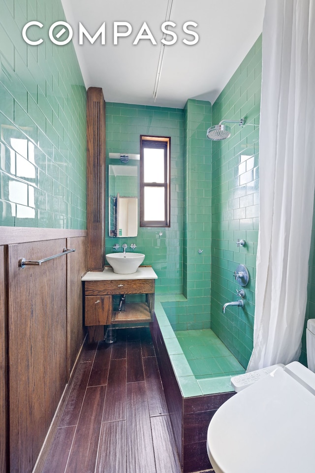 bathroom with tiled shower, toilet, a wainscoted wall, wood tiled floor, and vanity