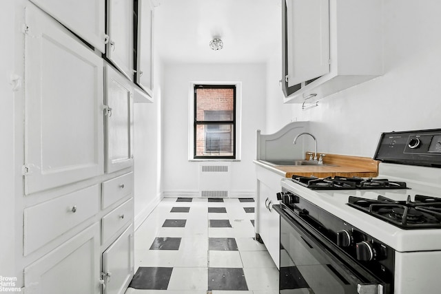 kitchen with range with gas cooktop, radiator, light countertops, white cabinetry, and a sink