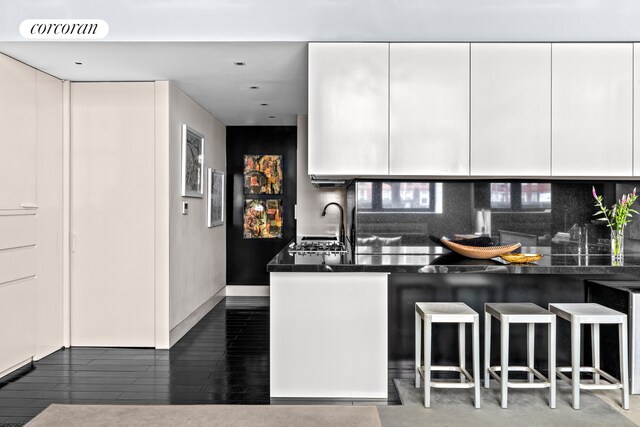 kitchen featuring dark countertops, a kitchen breakfast bar, decorative backsplash, modern cabinets, and white cabinets